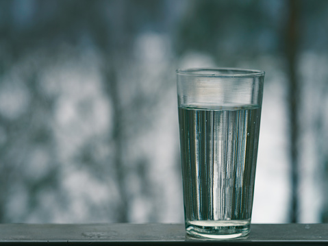 Conceptual photography of the glass  of water, Cold gray colors. Cool natural defocused background. Close up image