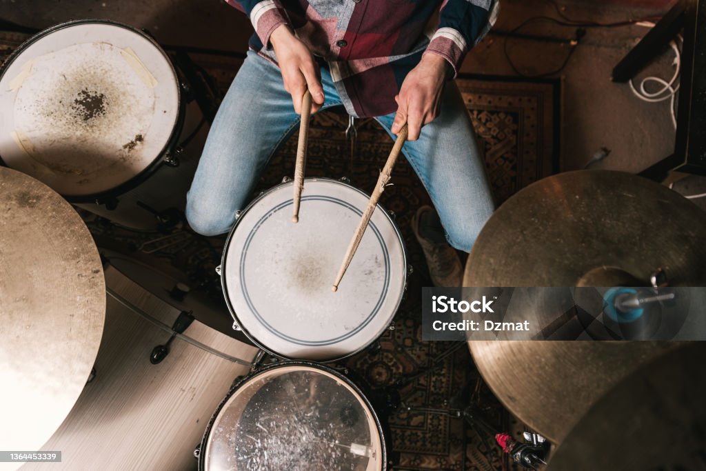 Man playing music on drum set in studio Top view of crop anonymous male musician in casual clothes playing acoustic drum kit during live performance Drummer Stock Photo
