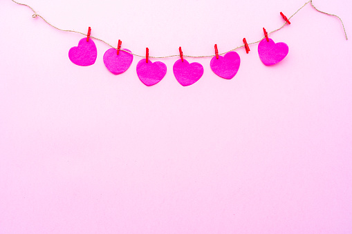 Valentines day background: several pink paper hearts hanging on a rope with clothespins shot on pink background. The composition is at the top of an horizontal frame leaving useful copy space for text and/or logo. High resolution 42Mp studio digital capture taken with SONY A7rII and Zeiss Batis 40mm F2.0 CF lens
