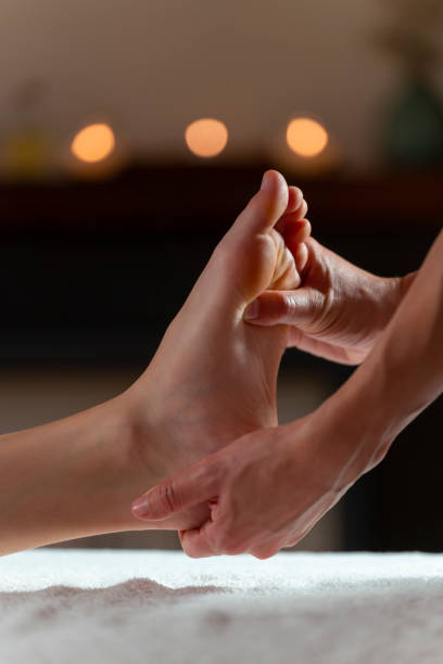 massaggiatore che fa un massaggio ai piedi con candele sullo sfondo - foot massage foto e immagini stock