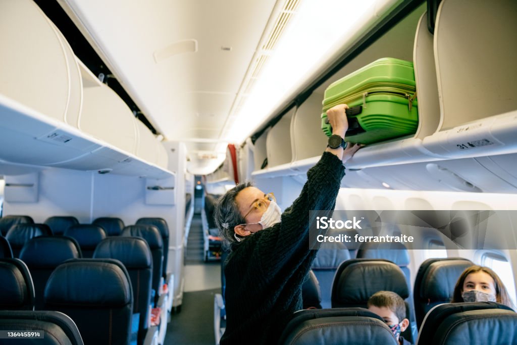 Family Air Travel Mother storing carry on luggage on airplane overhead bin Carry-On Luggage Stock Photo