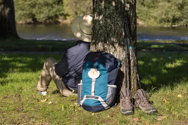 Scene of a Backpack leaning against a tree, boots and accessories and a pilgrim resting on his way to Santiago de Compostela. Camino de Santiago concept