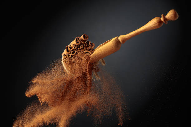 Cinnamon powder is poured out of the wooden spoon. Cinnamon powder is poured out of the wooden spoon. The ground cinnamon and cinnamon sticks, tied with jute rope on a black background. levitation stock pictures, royalty-free photos & images