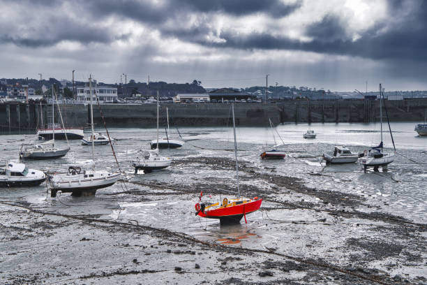 A grounded fiery red boat waits for the next high tide at the harbor of Grandville, Normandy in France.