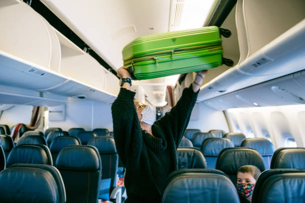 Family Air Travel Mother storing carry on luggage on airplane overhead bin hand luggage stock pictures, royalty-free photos & images