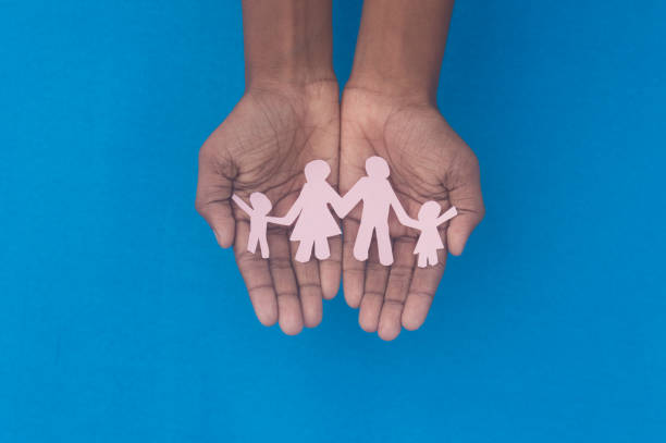 Hand holding family figure cutout top view. World health day Protection against domestic violence, healthcare and medical background. Foster care, homeless support and social distancing concept. Hand holding family figure cutout top view. World health day Protection against domestic violence, healthcare and medical background. Foster care, homeless support and social distancing concept. domestic violence india stock pictures, royalty-free photos & images
