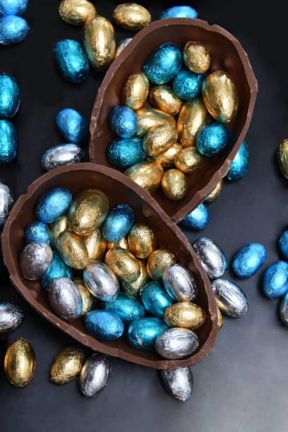 istock Pile of multi colored and different sizes of colourful foil wrapped chocolate easter eggs in blue, silver, and gold with two halves of a large brown milk chocolate egg in the middle and mini eggs inside. 1364466036