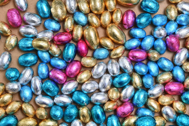 istock Large & small pink, blue, silver and gold foil wrapped chocolate easter eggs, against a pale wood background. 1364466246