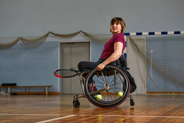 mujer joven discapacitada en silla de ruedas jugando al tenis en la cancha de tenis - wheelchair tennis physical impairment athlete fotografías e imágenes de stock