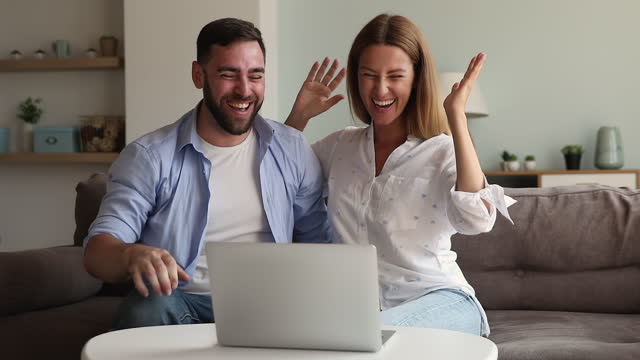 Young couple cuddle on sofa play online lottery using laptop