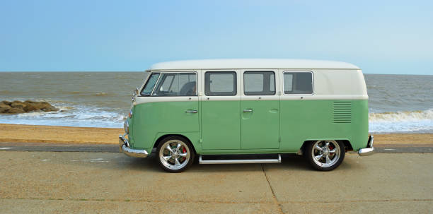 clásica furgoneta vw camper verde y blanca estacionada en el paseo marítimo. playa y mar al fondo - caravana de autobuses fotografías e imágenes de stock