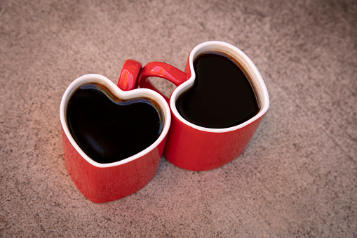 This is a photo of 2 heart shaped coffee cups sitting on a textured table.