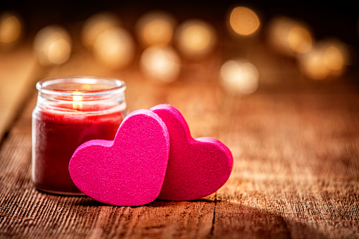 Burning candles with rose fresh flowers bouquet on gray table, close up home interior details with bokeh lights