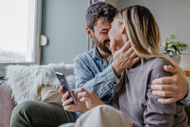 istock Young couple embracing at home and using mobile phone 1364484970