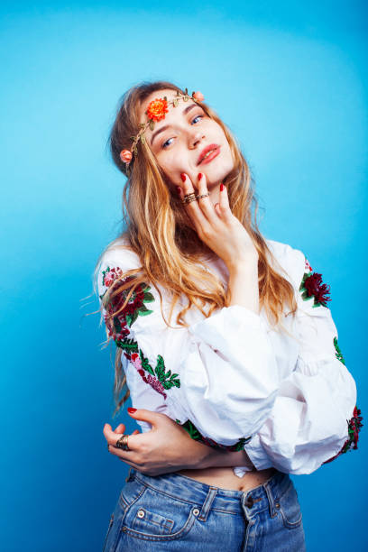 young pretty blond girl posing on blue background, fashion style hippie boho flowers on head stock photo