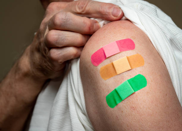 Senior man holding up shirt showing three covid-19 vaccine injections Senior caucasian man sleeve to show the third booster coronavirus vaccine shot in the shoulder. Concept with three separate bandages for the shots booster dose photos stock pictures, royalty-free photos & images