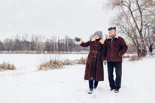 Senior family couple walking outdoors during snowy winter weather. Elderly people holding hands enjoying landscape. Valentine's day