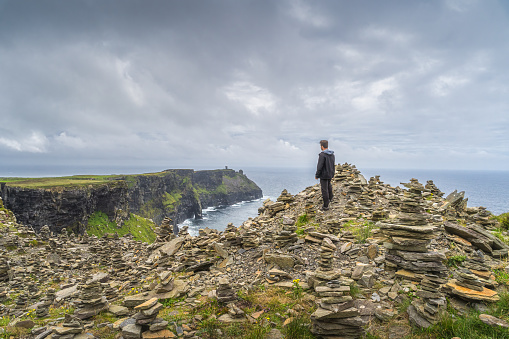 Man standing between stone stackings and admiring view on in iconic Cliffs of Moher, popular tourist attraction, Wild Atlantic Way, Co. Clare, Ireland
