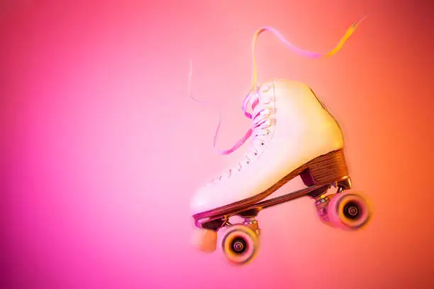 Classic white leather roller skate levitating on the pink and orange background. Sports equipment and recreation. Dynamic horizontal pop art poster. Layout with free copy (text) space.
