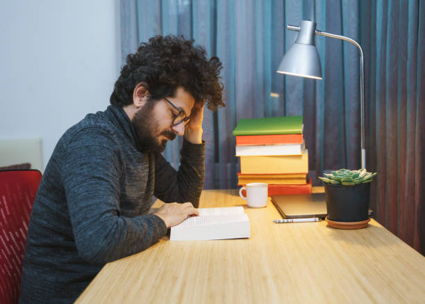 istock Man working on laptop at his desk, He is reading book 1364492631