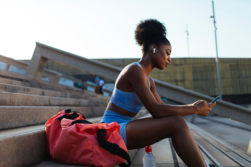 Young fit African American woman using her cellular phone before starting her workout