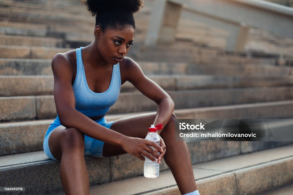 Ready to continue her workout Young fit woman sitting on a set of stairs while drinking water during a workout break African-American Ethnicity Stock Photo