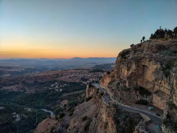 Panoramic view of a rocky hill crossed by a road, houses scattered below and mountains on the horizon. Constantine, Algeria