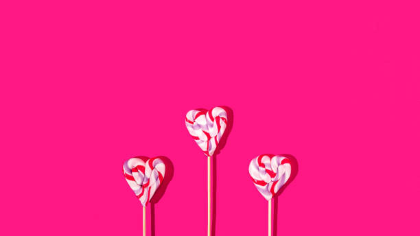 istock Thre colorful heart shaped lollipops on bright magenta background. Creative concept for Valentine day card or banner or for wedding invitation. Artistic design for mother's day advertisement. 1364495887