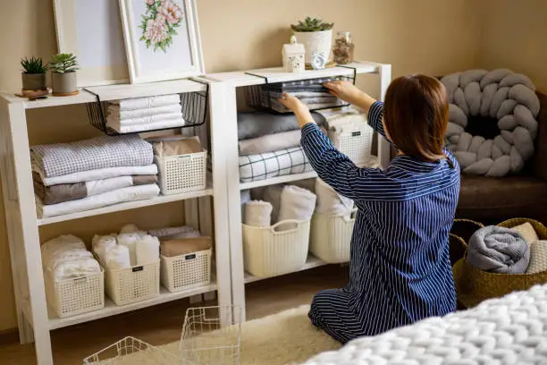 Photo of Domestic woman in pajamas neatly putting folded linens into cupboard vertical storage Marie Kondo