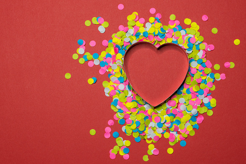 Heart-shaped paper puncher confetti scattered on a red background. Valentine LOVE concept.