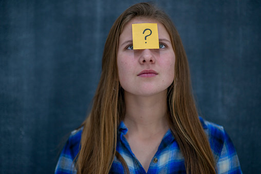 A high school girl looks up with ambition toward a post it note that has a question mark symbol on it.