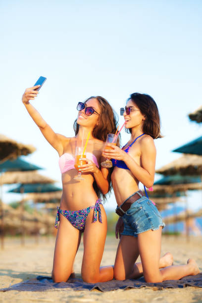 due ragazze sexy che si prendono selfy su una spiaggia - umbrella beach sex symbol white foto e immagini stock