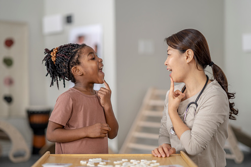 A therapist guides a young girl through speech therapy exercises using a playful and modern approach.