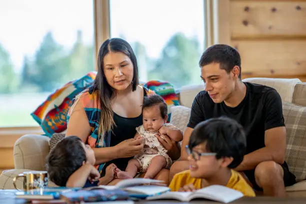 A mother and her kids hang out in their living room, smiling as they take care of the baby of the family.