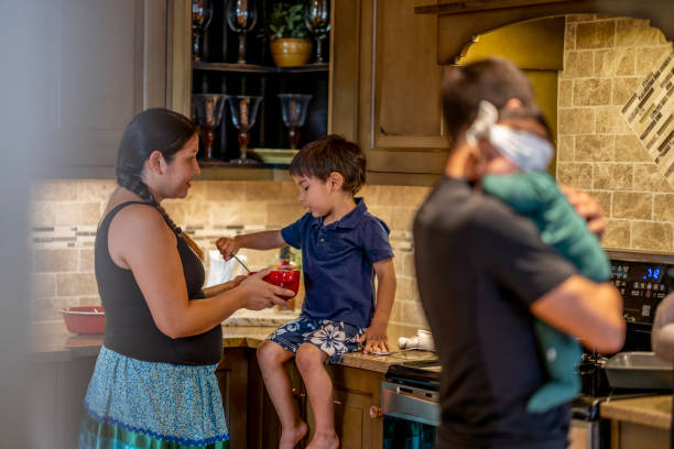 A woman shows her kids what she is making in the kitchen.