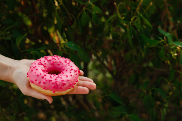 istock Girl holding an appetizing pink donut in her hand 1364515929