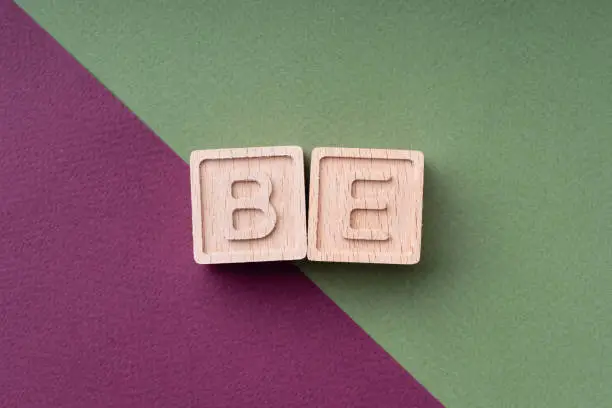 Photo of BE is a word made up of wooden cubes on a scarlet and green background. The phrase calls for action, the slogan. A bright creative concept. Be who you want to be