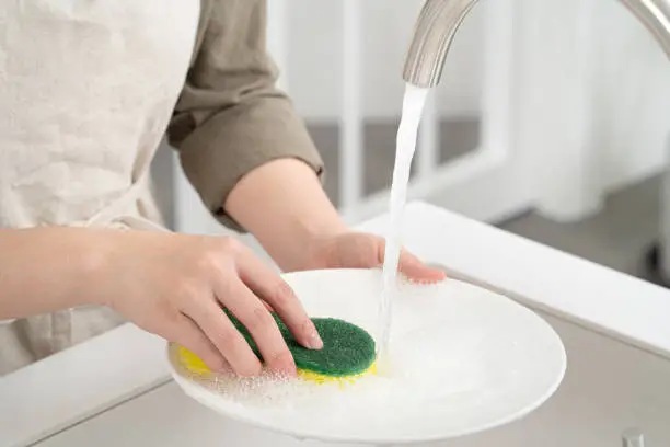 Close up of woman housekeeper is doing the dishes at home kitchen by using wash sponge and dishwashing.