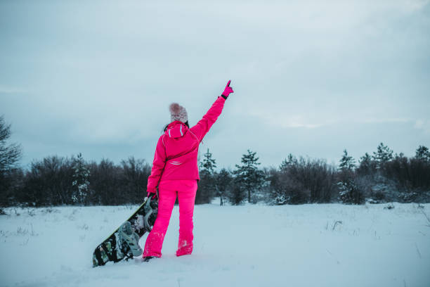 A young woman holds a snowboard. View from behind
