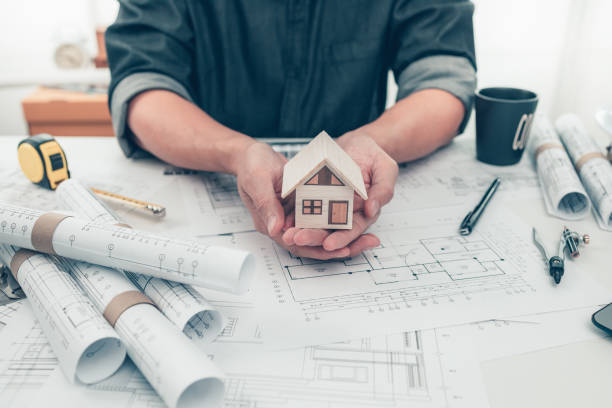 istock Architect engineer hands hold and show mini house model and use pen drawing on blueprint. House planning design and construction concept. 1364535818