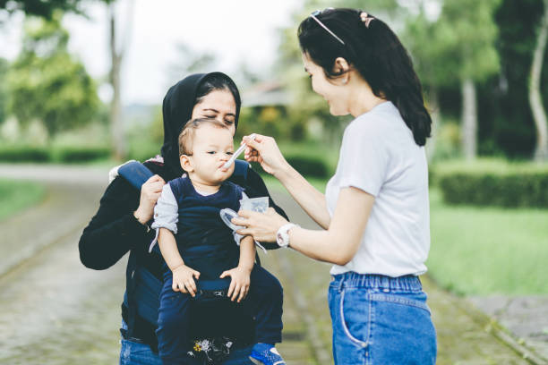 mother feeding her baby when grandmother carrying the baby - baby carrier fotos imagens e fotografias de stock