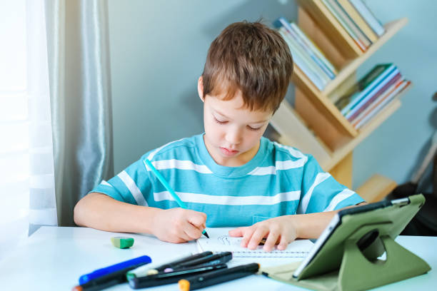 istock Caucasian boy sits at table with digital tablet and draws drawing with markers. Using modern gadgets and Internet for home and distance education. 1364538655