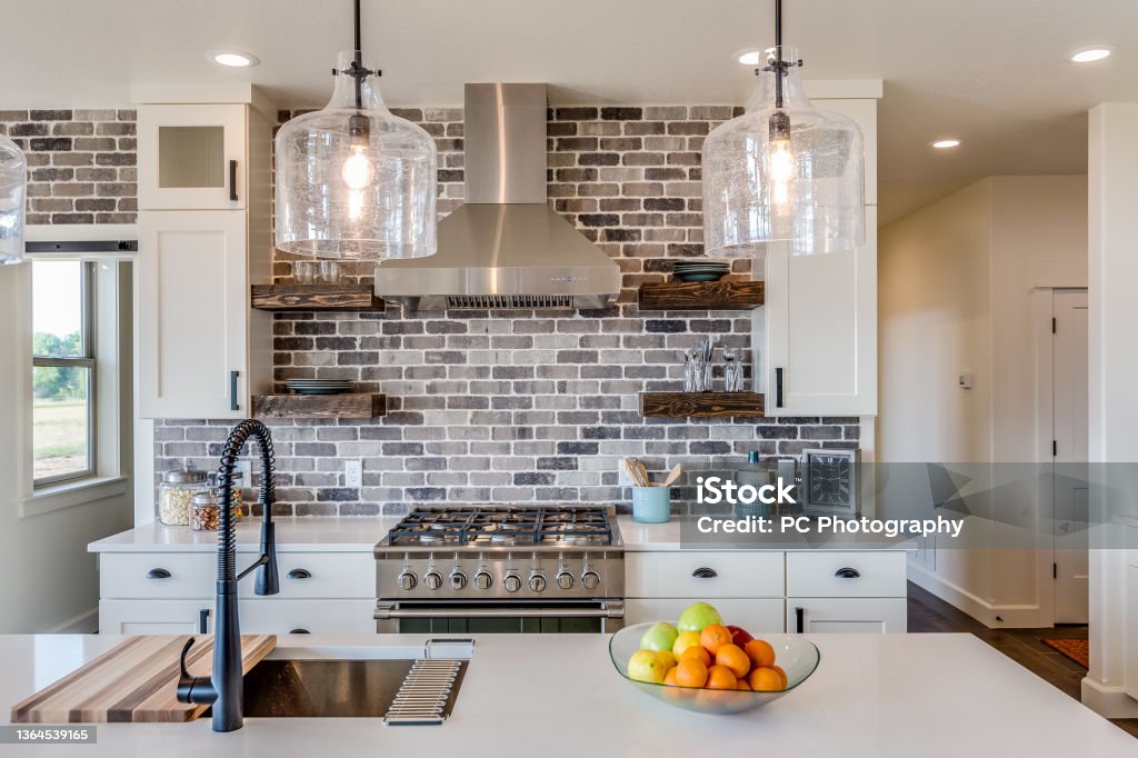 Gorgeous kitchen with vent hood and brick backsplash Sink and black faucet on island with two pendant lights overhead Kitchen Stock Photo