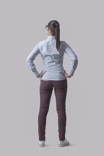 Young woman standing full body back view, isolated on gray background