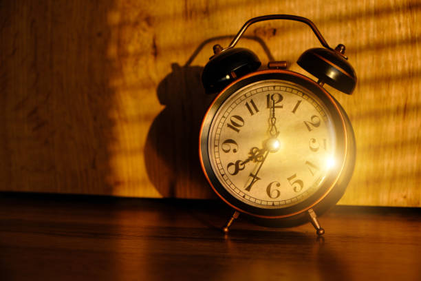 istock Old retro alarm clock in early morning on table, shadows from blinds on background. 1364541754