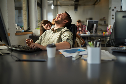 Cheerful male programmer having fun while being scared by his colleague in the office.