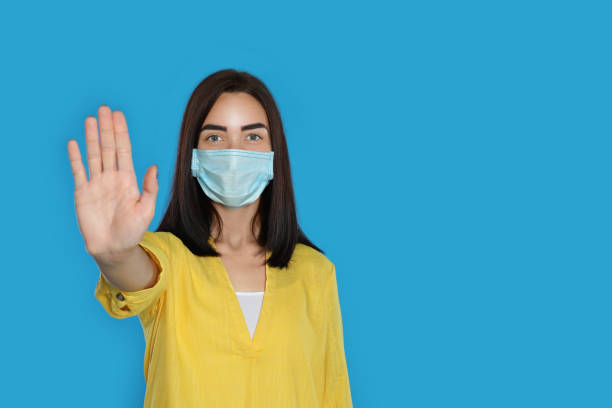 istock Young woman in protective mask showing stop gesture on light blue background, space for text. Prevent spreading of coronavirus 1364545018