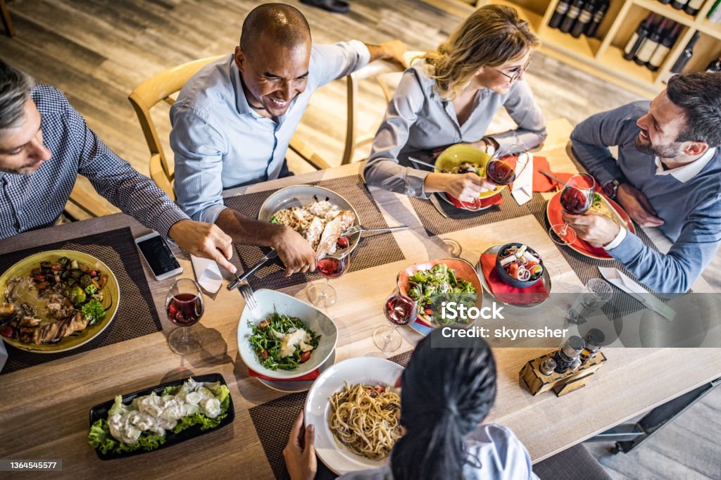 Above view of group of happy business people talking on a lunch. High angle view of happy business colleagues talking on a lunch break in a restaurant. Business Lunch Stock Photo