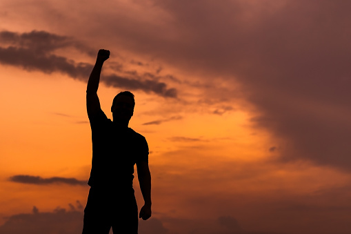 Silhouette of a man with hands raised in the sunset, empowered concept.