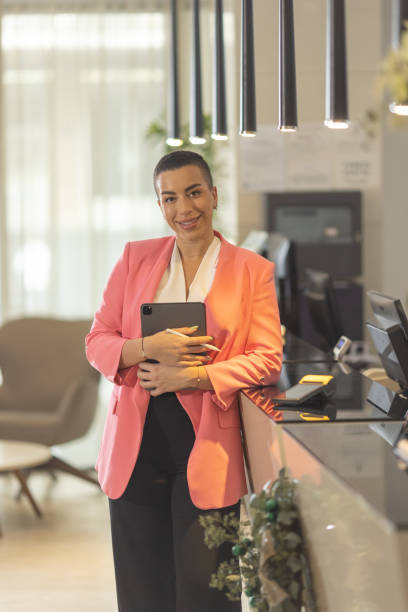 istock Short haired female receptionist standing in hotel lobby with tablet in hands 1364550080